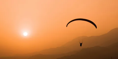 A paraglider in silhouette against an orange sunset